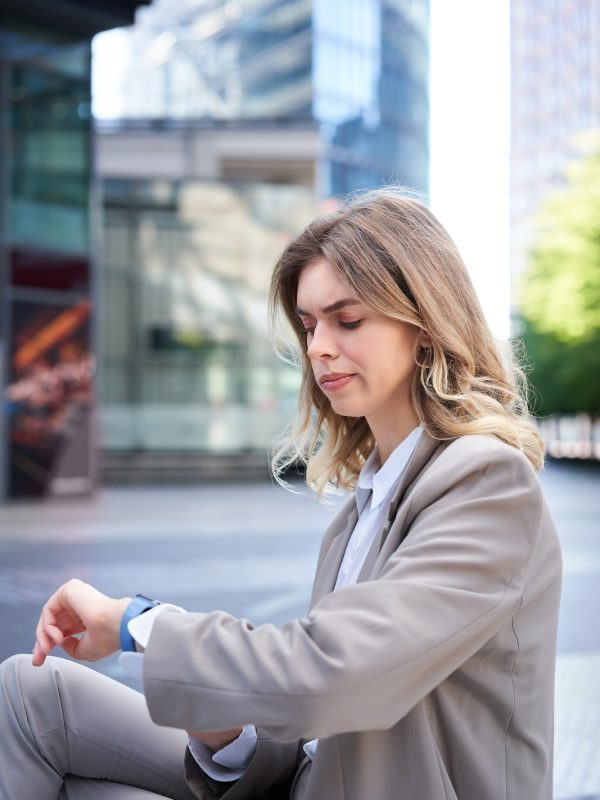 frowning-businesswoman-in-suit-looking-at-her-digital-watch-with-disappointed-face-annoyed.jpg